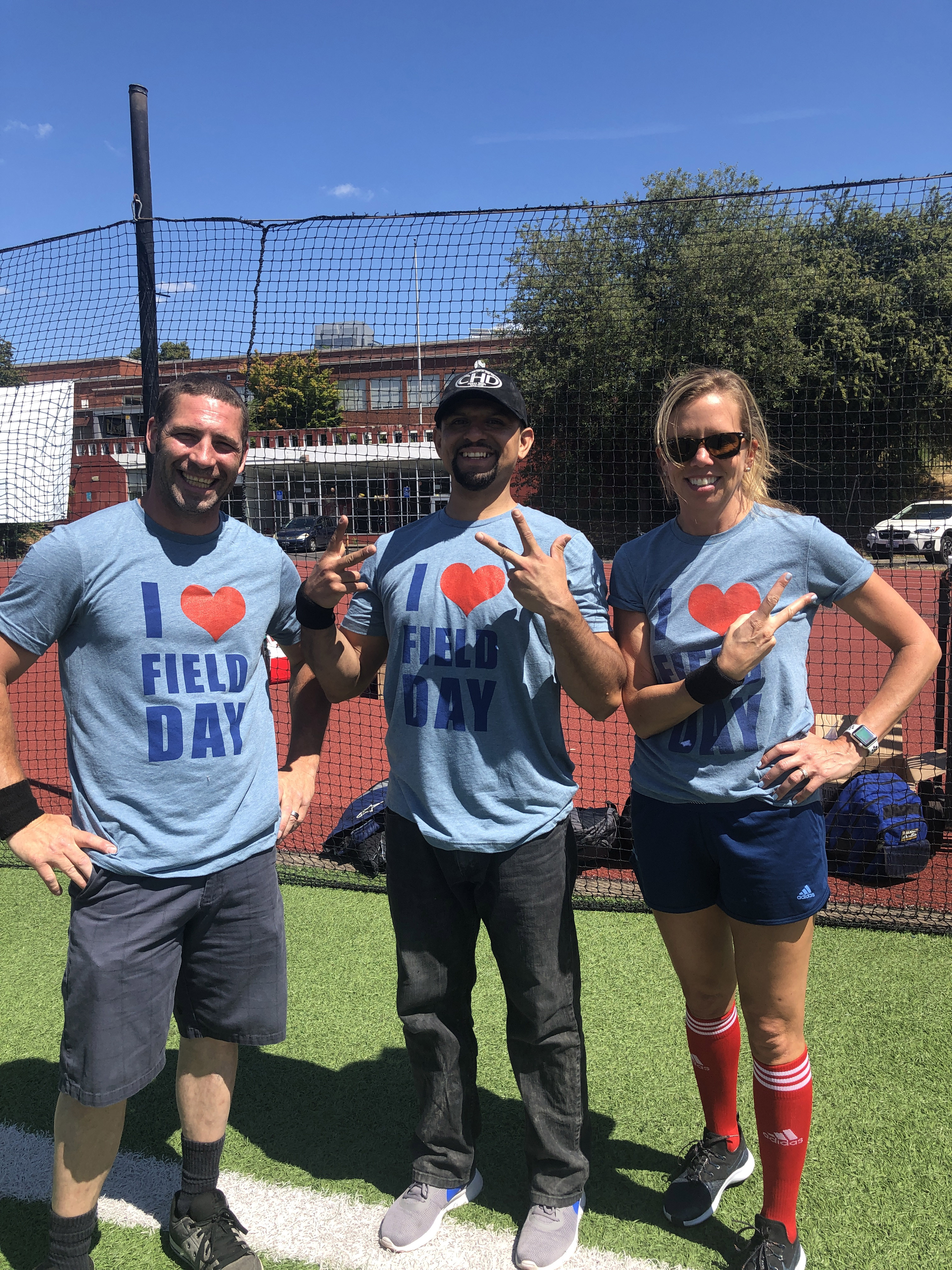 Three R&H employees posing in custom t-shirts for R&H field day on the football field